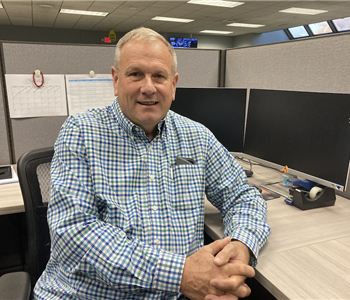 owner Kevin smiling in blue plaid shirt at desk