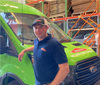 Brendan posing with arm on SERVPRO Van in a blue shirt and hat