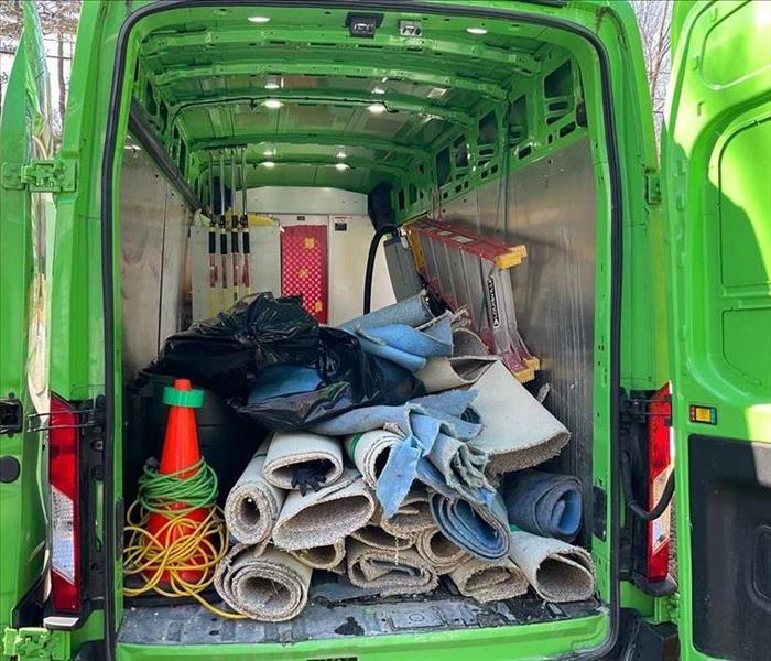 A green SERVPRO vehicle packed with trash bags of carpeting and pad for disposal, as well as SERVPRO mop heads and ladders
