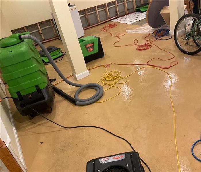 A wet floor, partially demolished wall, and some contents are shown near operational SERVPRO air movers and dehumidifiers